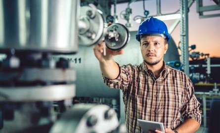 Person wearing hard hat in plant reading a gauge