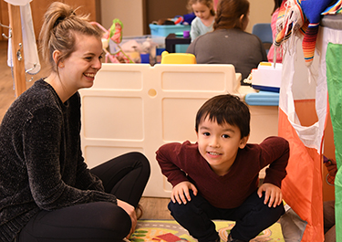  A child in the preschool room poses with a student.