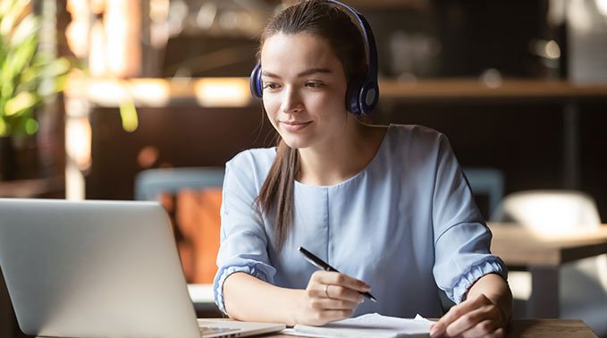 A woman wearing headphones studies from a laptop.